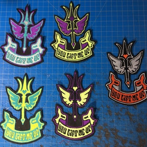 May include: Five embroidered patches with a central design of a stylized sword and wings, in various color schemes including purple, yellow, and teal. Each patch has the text "YOU LIFT ME UP" on a banner.