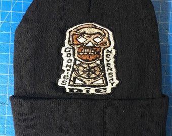 May include: Black knit beanie with a brown and white embroidered patch featuring a skull with the text "Goonies Never Say Die".