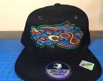 May include: Black baseball cap with a colorful paisley design embroidered on the front. The cap has a black snap closure and a black label with the text "Pit Bull Snapback" and a small image of a bull's head.