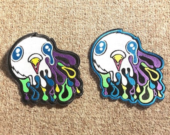 May include: Two embroidered iron-on patches featuring a cartoon character with a white face, blue eyes, and a yellow beak. The character is melting into a colorful liquid with purple, blue, green, and yellow drips.