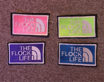 May include: Four embroidered patches with the text "The Flock Life" in white lettering on a black background. The patches are in pink, green, blue, and light blue.