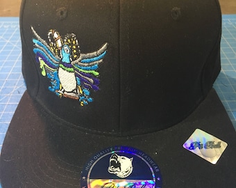 May include: Black baseball cap with a blue, green, and yellow embroidered design of a bird on the front. The cap has a black brim and a white label with the text "Pit Bull Snapback High Quality Premium Headwear" on the underside of the brim.