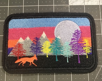 May include: Embroidered patch with a colorful sunset scene over mountains and a full moon. A fox silhouette is in the foreground. The patch is black with a white border.