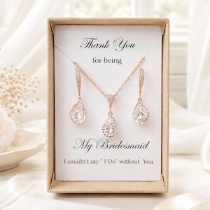 May include: A rose gold jewelry set featuring a necklace and two drop earrings with clear teardrop-shaped stones. The set is displayed in a cardboard box with the text: Thank You for being My Bridesmaid I couldn't say " I Do" without You.
