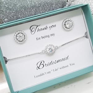 May include: A white gift box with a teal lid, containing a silver bracelet and earrings with clear stones. The box has a message that reads "Thank you for being my Bridesmaid. I couldn't say "I do" without you."