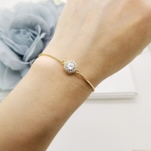 May include: A delicate gold chain bracelet with a single round clear crystal surrounded by smaller crystals.