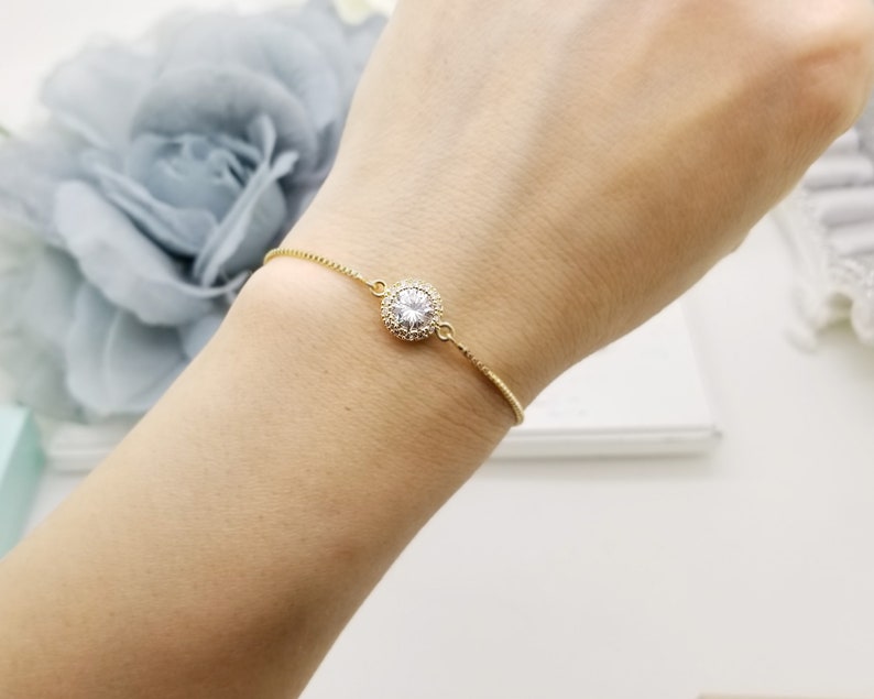 May include: A delicate gold chain bracelet with a single round clear crystal surrounded by smaller crystals.