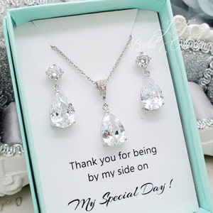 以下が含まれることがあります： 涙型の透明なクリスタルをあしらったシルバーのネックレスとイヤリングのセット。ジュエリーは、明るいブルーの箱に入っていて、「私の特別な日に側にいてくれてありがとう！」というメッセージが書かれています。