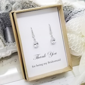May include: A small gift box with a white card that says "Thank You for being my Bridesmaid". The box contains a pair of silver teardrop earrings with clear cubic zirconia stones.