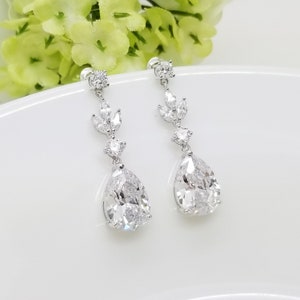 May include: A pair of silver teardrop earrings with clear cubic zirconia stones. The earrings feature a delicate leaf design with smaller stones.