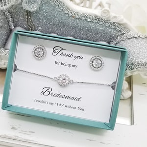 May include: A teal gift box with a white card inside. The card says "Thank you for being my Bridesmaid. I couldn't say "I do" without you." The box contains a silver bracelet and a pair of silver earrings with clear stones.