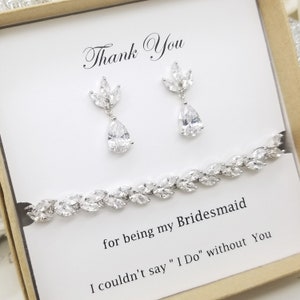 May include: A white card with the text "Thank You" and "for being my Bridesmaid I couldn't say "I Do" without You" in black lettering. The card is in a box with a silver bracelet and earrings with clear stones.