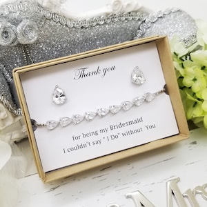 Könnte beinhalten: Ein Geschenkset mit einem silbernen Armband und passenden Ohrringen, jeweils mit klaren, birnenförmigen Kristallen. Das Set wird in einer kleinen, hellbraunen Schachtel mit einer Karte präsentiert, die lautet: "Thank you for being my Bridesmaid. I couldn't say 'I Do' without You."