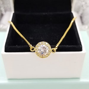 May include: A gold chain bracelet with a large, clear, round cubic zirconia stone surrounded by smaller stones.