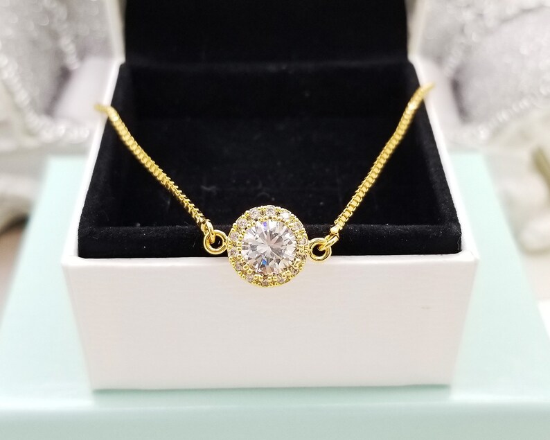 May include: A gold chain bracelet with a large, clear, round cubic zirconia stone surrounded by smaller stones.