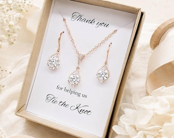 May include: A rose gold necklace and matching drop earring set featuring clear round stones, presented in a kraft paper box with a white card printed with the text Thank you for helping us Tie the Knot in black script and serif fonts.