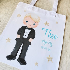 May include: White tote bag with a cartoon illustration of a young boy in a tuxedo. The bag has the name "Theo", the words "page boy", and the date "19/07/25" in teal, with gold glitter stars scattered around.