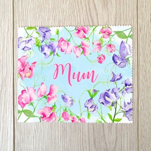 Peut inclure: Carte florale avec un fond bleu clair et le mot "Mum" en rose. Des fleurs de pois de senteur roses et violettes et des vignes vertes encadrent le texte. La carte a un bord festonné décoratif.