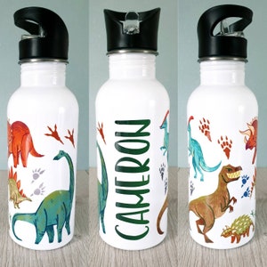 Peut inclure: Bouteille d'eau blanche avec un bouchon noir, orn&eacute;e d'illustrations de dinosaures color&eacute;s et du nom "CAMERON" en vert. Les dinosaures sont de couleurs rouge, vert, marron et bleu, avec des empreintes de pattes.