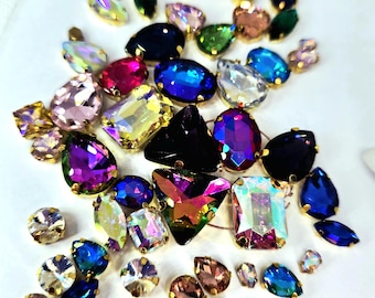 May include: A collection of colorful rhinestones in various shapes and sizes, including oval, teardrop, and geometric forms. The rhinestones feature a gold-colored metal backing and a range of colors, such as blue, pink, green, and iridescent.