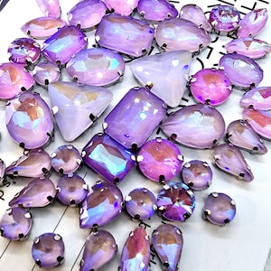 May include: Assortment of iridescent purple and pink rhinestones in various shapes and sizes. The rhinestones have a silver backing and are perfect for crafting and jewelry making.