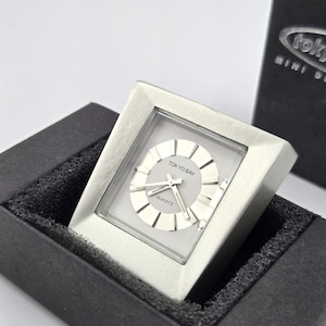 May include: A silver-toned Tokyo Bay Quartz watch with a square face, displayed in a black box. The watch face is light gray with silver hands and markers. The watch is labeled "TOKYO BAY QUARTZ".