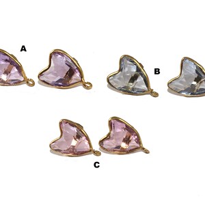 Pode incluir: Três pares de brincos de cristal em forma de coração com engastes dourados. Os brincos estão em três cores: rosa claro, rosa escuro e transparente.
