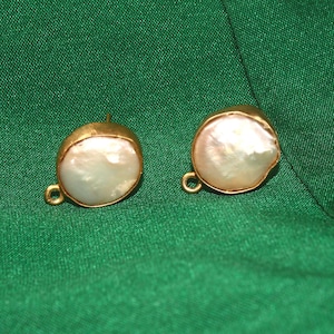 May include: A pair of gold-tone earrings with a white pearl-like center. The earrings are on a green fabric background.