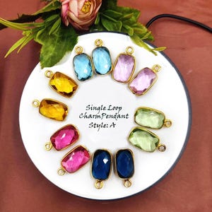 May include: Assortment of single loop charm pendants in various colours, including blue, green, pink, and yellow. The pendants are displayed on a white plate with the text "Single Loop Charm Pendant Style: A".