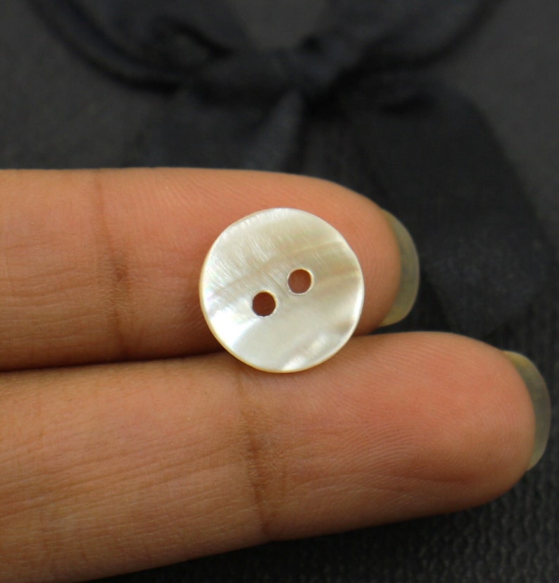 May include: A white mother of pearl button with two holes.