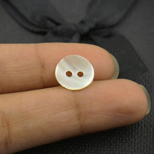May include: A white mother of pearl button with two holes.