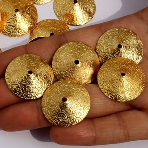 May include: A collection of gold-colored metal embellishments with a decorative floral pattern. The embellishments are round and have a small hole in the center.