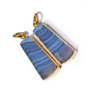 May include: Two blue agate pendants with gold-plated edges. The pendants are rectangular in shape and have a natural, striated pattern.