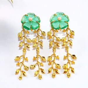 Puede incluir: Pendientes de oro con detalles de cristal verde en forma de flor y perlas. Los pendientes tienen un dise&ntilde;o colgante con m&uacute;ltiples hojas doradas.