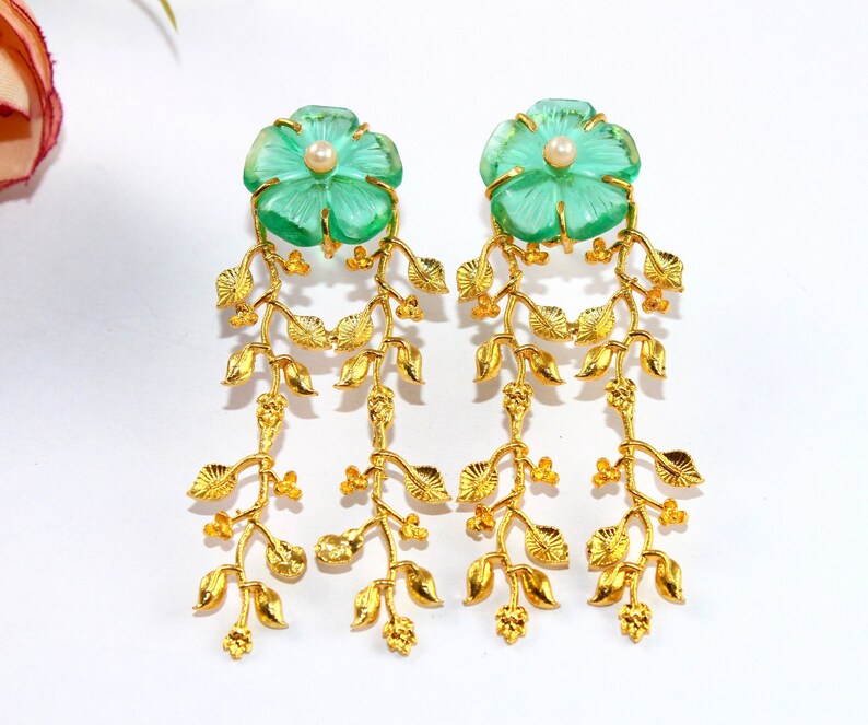 Puede incluir: Pendientes de oro con detalles de cristal verde en forma de flor y perlas. Los pendientes tienen un dise&ntilde;o colgante con m&uacute;ltiples hojas doradas.