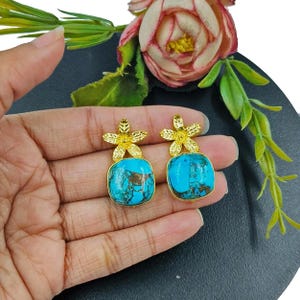 Puede incluir: Un par de pendientes de oro con piedras turquesa y detalles en forma de flor.