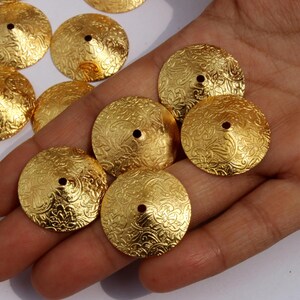 May include: A collection of gold-toned metal embellishments with a decorative, embossed pattern. The embellishments are round and have a raised center.
