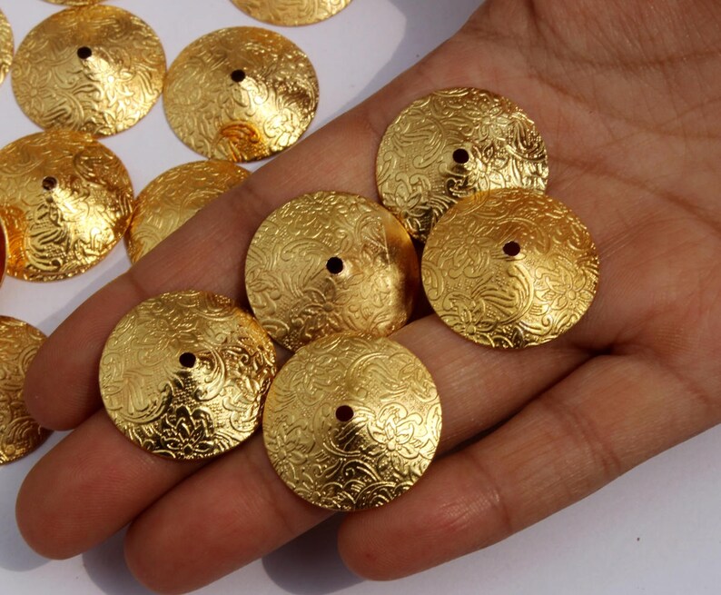 May include: A collection of gold-toned metal embellishments with a decorative, embossed pattern. The embellishments are round and have a raised center.