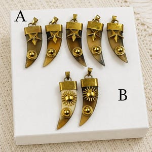 May include: Seven horn-shaped pendants with gold-toned metal caps and accents. Five pendants in group A feature a five-pointed star and a small circular stud. Two pendants in group B feature a sunburst emblem and a small circular stud.