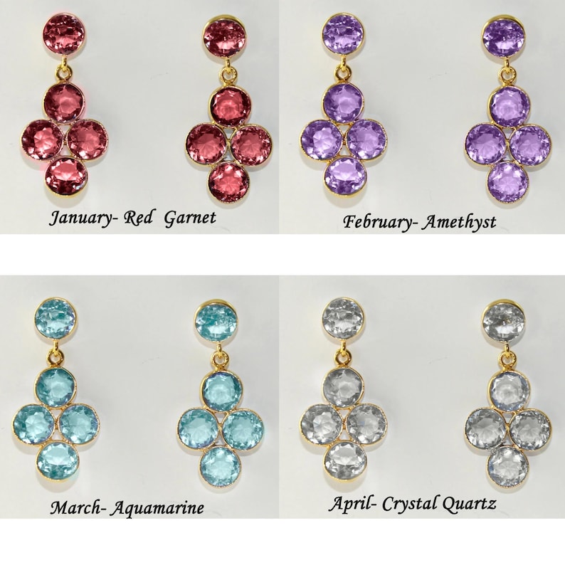 May include: Four pairs of dangle earrings with a cluster of five round gemstones. The earrings are in red, purple, blue, and clear. The text below each pair of earrings reads "January-Red Garnet", "February-Amethyst", "March-Aquamarine", and "April-Crystal Quartz".