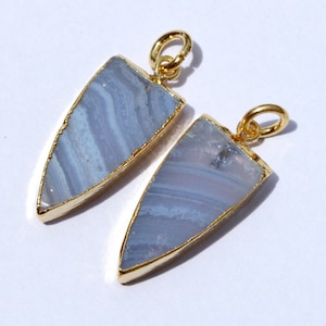 Può includere: Due ciondoli in agata blu pizzo con finiture color oro e un anello per appenderli. I ciondoli hanno una forma triangolare con la parte superiore arrotondata e la parte inferiore a punta. L'agata blu ha un motivo a strati.