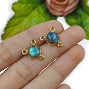 Könnte beinhalten: Zwei goldfarbene Metall-Verbindungsanhänger mit einem runden, schillernden blauen Labradorit-Edelstein in der Mitte. Jeder Anhänger hat drei Schlaufen zum Anbringen an Schmuck.