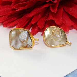 May include: Two gold-toned metal charms with a white iridescent shell inlay. The charms have a loop on the side for attaching to jewelry.