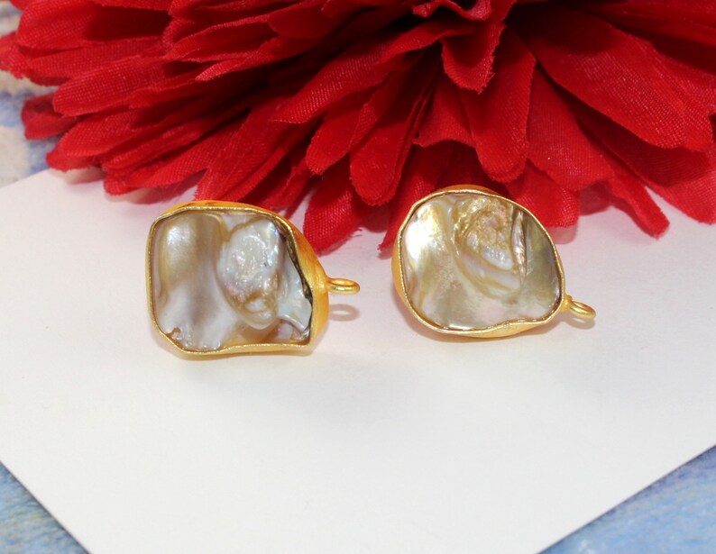 May include: Two gold-toned metal charms with a white iridescent shell inlay. The charms have a loop on the side for attaching to jewelry.