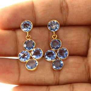 May include: A pair of gold dangle earrings with blue gemstone drops. The earrings feature a cluster of five round blue gemstones.