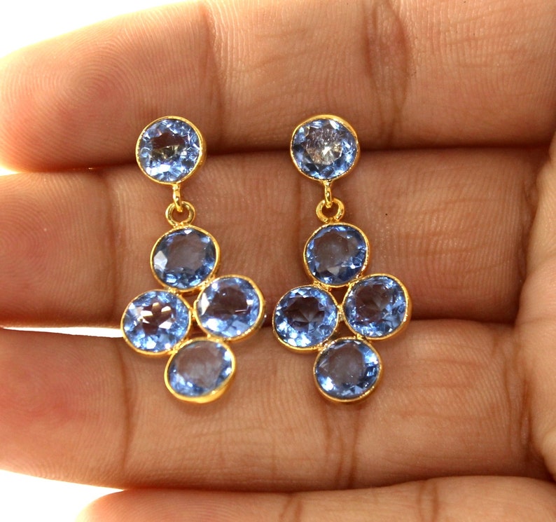 May include: A pair of gold dangle earrings with blue gemstone drops. The earrings feature a cluster of five round blue gemstones.