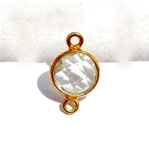 Puede incluir: Conector dorado con una piedra preciosa redonda facetada transparente. El conector tiene dos bucles en la parte superior e inferior para sujetar joyas.