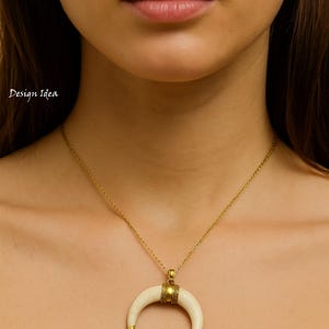 May include: A gold necklace featuring a crescent moon pendant. The pendant is off-white with gold tips and a gold band. The necklace is worn around the neck.