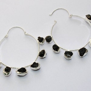 May include: Silver hoop earrings with black gemstone accents. The earrings have a simple, modern design and are perfect for everyday wear.