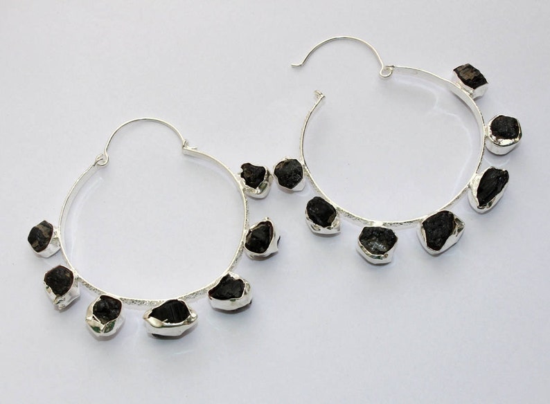 May include: Silver hoop earrings with black gemstone accents. The earrings have a simple, modern design and are perfect for everyday wear.